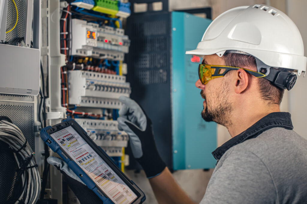 Man, an electrical technician working in a switchboard with fuses. Installation and connection of electrical equipment. Professional uses a tablet.